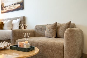 Ett modernt vardagsrum med en beige soffa, ett runt soffbord i trä med dekorativa föremål och en tavla på väggen.