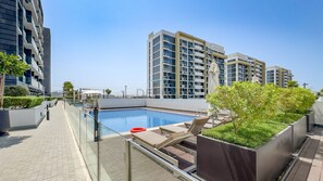 A rooftop swimming pool with lounge chairs and a glass balustrade. - Modern Layout Studio,Smooth Drive from Nad Al Sheba Stadium & Meydan Racecourse (Dubai)