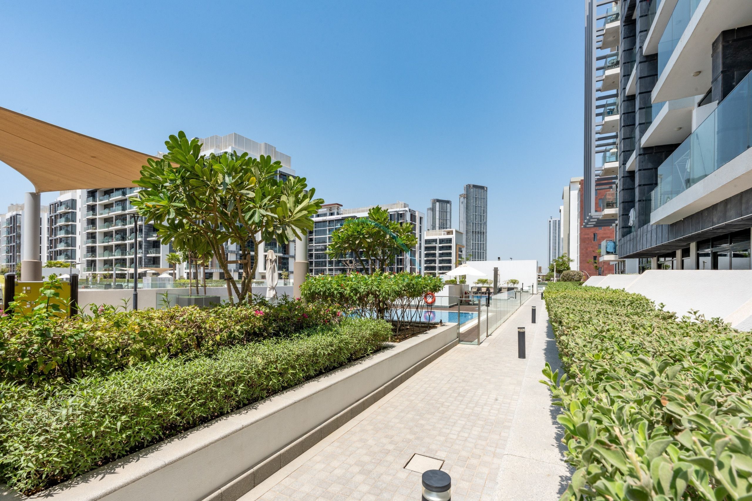 A modern urban landscape with high-rise buildings, a landscaped pathway, and a pool area.