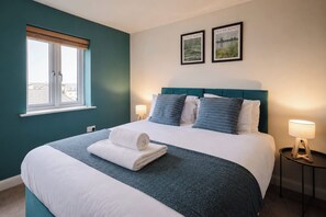 Habitación de hotel con una cama, dos lámparas de noche, una ventana con persianas y dos cuadros en la pared.