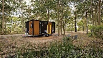 A small cabin with a door, a table, and chairs outside, surrounded by trees and vegetation.