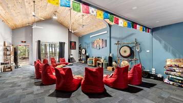 A room with a high ceiling, wooden beams, red bean bags, a drum set, and colorful prayer flags.