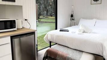 A bedroom with a bed, a desk, a microwave, and a small refrigerator.