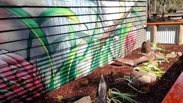 A garden with a colorful mural on a wooden wall, a wooden bench, and a small rock garden.