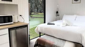 A bedroom with a bed, a desk, a microwave, and a small refrigerator.