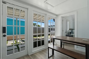 A room with a wooden floor, a dark wooden table, and a bench. There are white-framed windows and a door. - 5 Min to Vanderbilt Beach Pet Friendly 3BR (Naples)