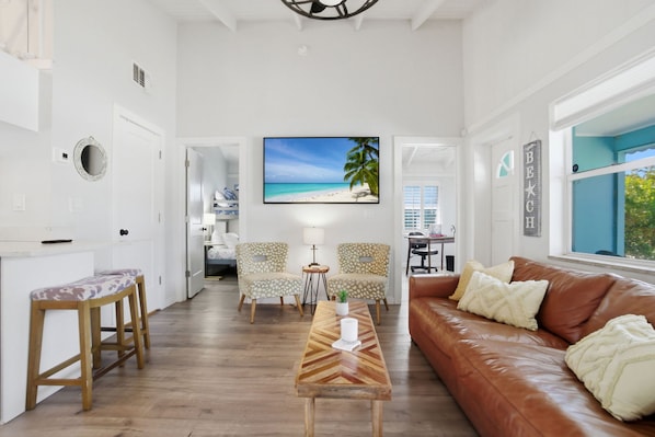A spacious living area with a wooden coffee table, a brown leather sofa, and two patterned chairs. A large window provides a view of the outdoors. - 5 Min to Vanderbilt Beach Pet Friendly 3BR (Naples)