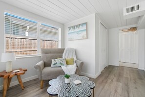 A room with a grey armchair, a white fluffy throw, a small table with a plant, and a painting of a beach scene. - 5 Min to Vanderbilt Beach Pet Friendly 3BR (Naples)