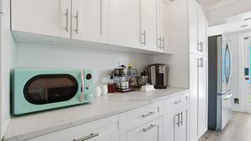Una cocina con armarios blancos, un microondas verde azulado, una cafetera y un refrigerador.