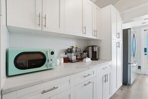 A kitchen with white cabinets, a teal-colored microwave, a coffee maker, and a refrigerator. - 5 Min to Vanderbilt Beach Pet Friendly 3BR (Naples)