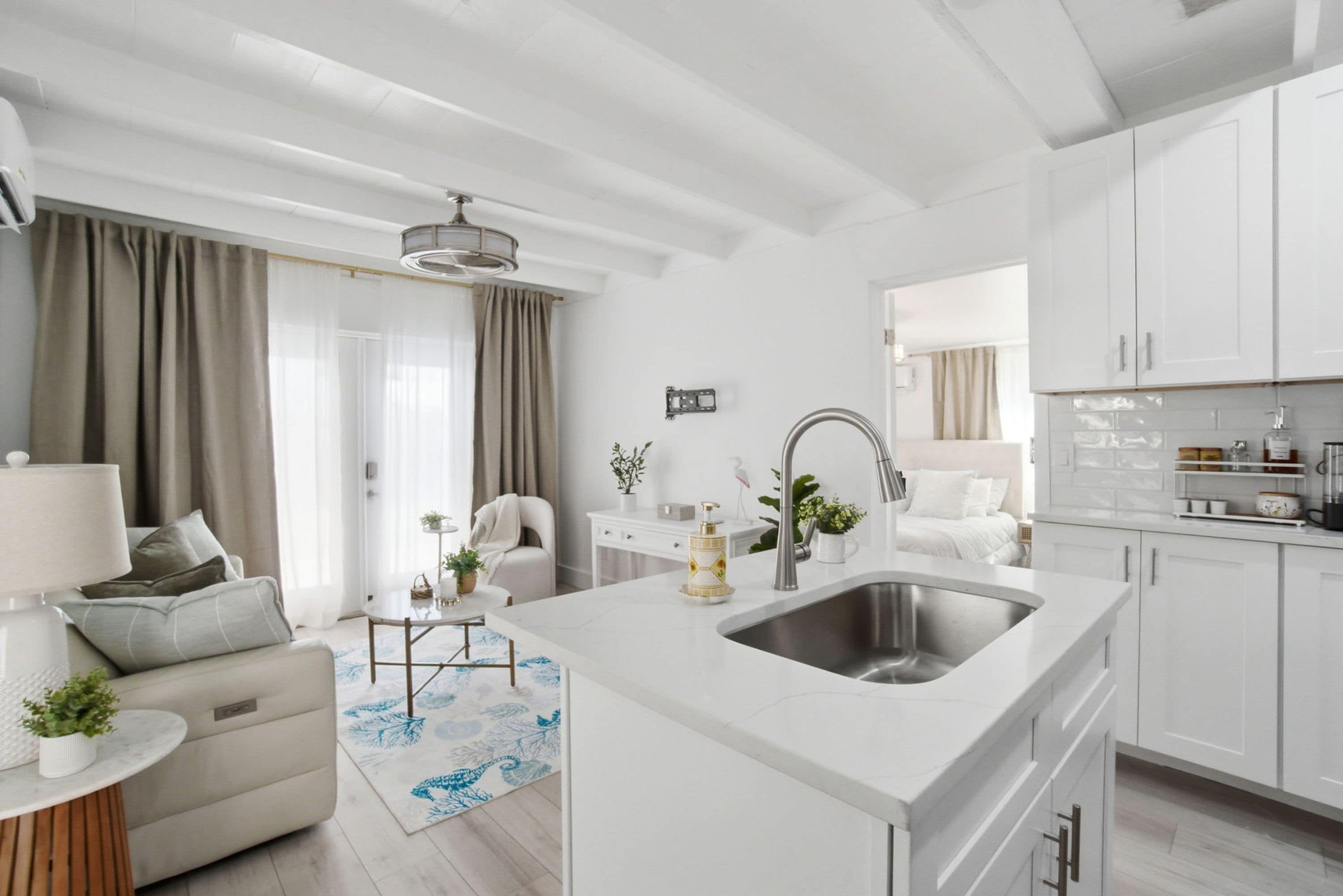 A modern kitchen with white cabinetry, a central island with a sink, and a dining area with a table and chairs.