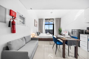 Ein modernes Hotelzimmer mit einer Sitzecke, einem Esstisch mit Stühlen, einem Bett, einem Feuerlöscher und Blick auf die Stadt.