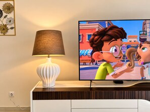 A television displaying animated characters, a white lamp, and a wall with a framed floral design. - Atlantic Pearl Apartment Sea View Family Retreat in Canico (Santa Cruz)