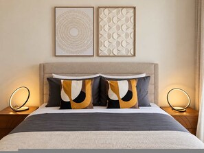 A neatly made bed with a grey and white duvet, two decorative pillows with abstract patterns, and two wall-mounted light fixtures on either side. - Atlantic Pearl Apartment Sea View Family Retreat in Canico (Santa Cruz)