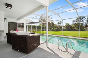 A covered outdoor area with a pool, wicker furniture, and a view of the surrounding greenery. - Naples Pool Home 10 Min to Naples Zoo (Naples)
