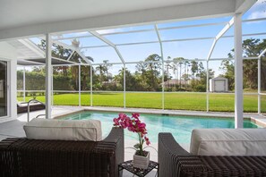 A covered outdoor pool area with wicker furniture and a view of a green lawn. - Naples Pool Home 10 Min to Naples Zoo (Naples)