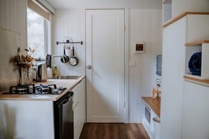 A compact kitchen with white cabinetry, a stove, a sink, and a window. - Tiny House for Glamping Escape in Dadswells Bridge, Victoria (Dadswells Bridge)