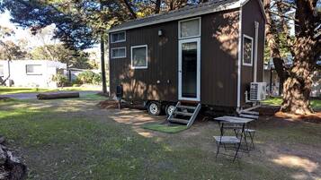 A small, single-story mobile home with a ramp leading to the door, situated in a grassy area with trees in the background.