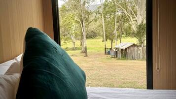A bedroom with a bed, a pillow, and a view of a grassy area with trees and a wooden structure.