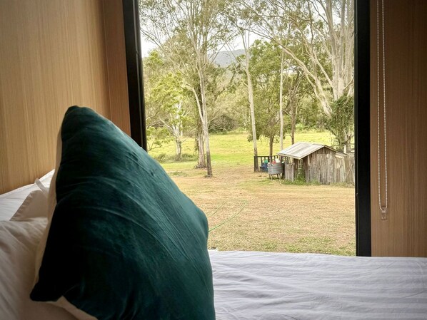 A bedroom with a bed, a pillow, and a view of a grassy area with trees and a wooden structure.