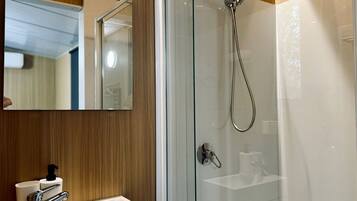 A modern bathroom with a glass-enclosed shower, a white sink with a soap dispenser, and a mirror above the sink.