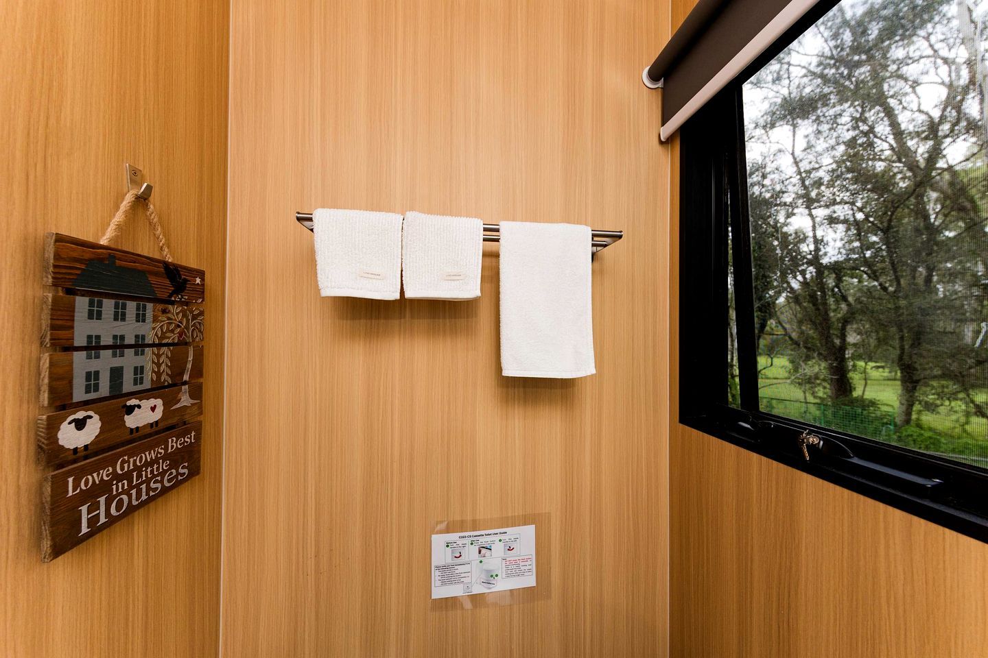 A wooden wall with a window, two white towels hanging on a towel rack, and a wooden sign with a house and sheep illustration.