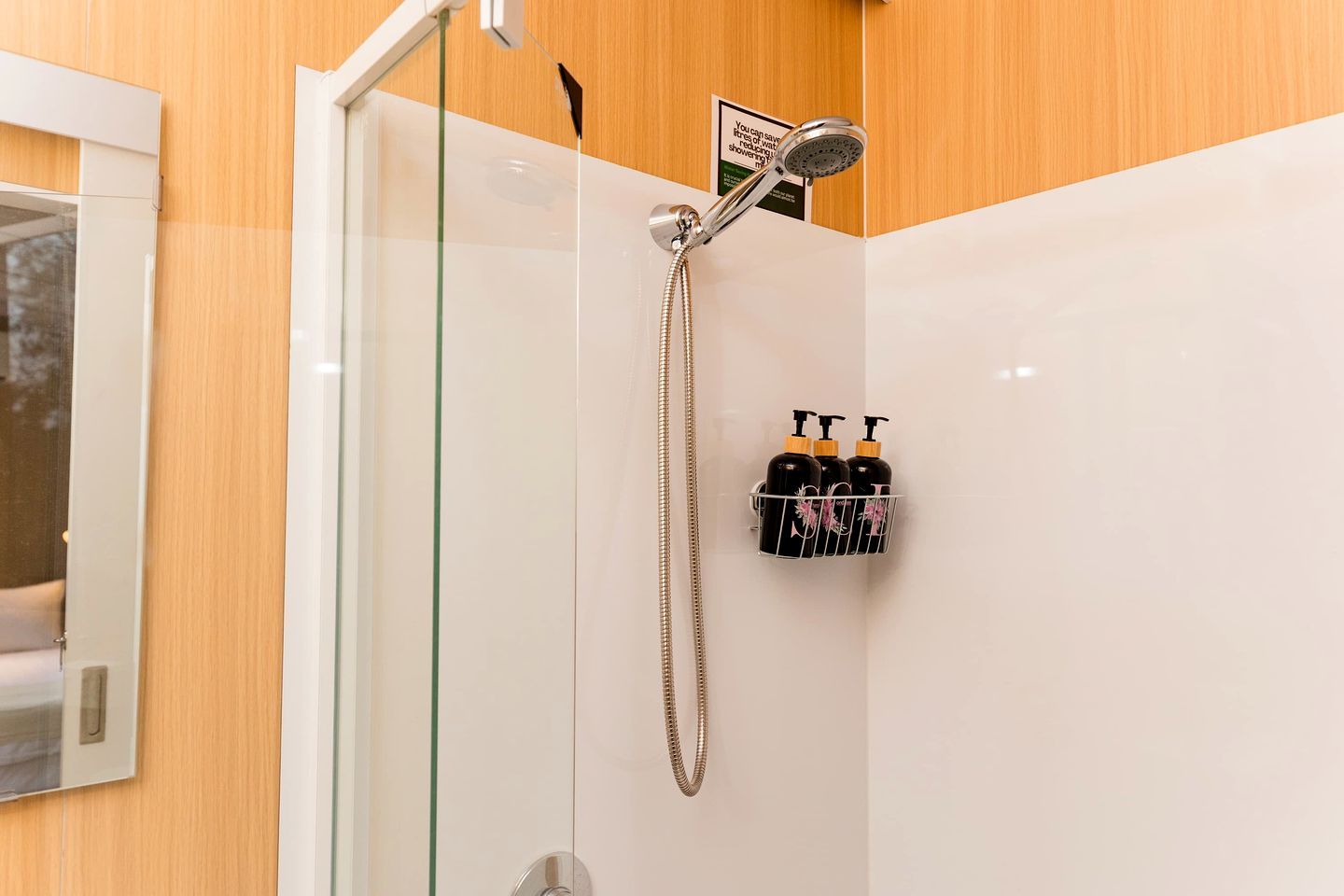 Eine Dusche mit Handbrause und Wandarmatur, eine Glasduschwand und ein Ablagerost mit drei Shampoo-Flaschen.