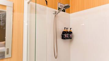 Eine Dusche mit Handbrause und Wandarmatur, eine Glasduschwand und ein Ablagerost mit drei Shampoo-Flaschen.