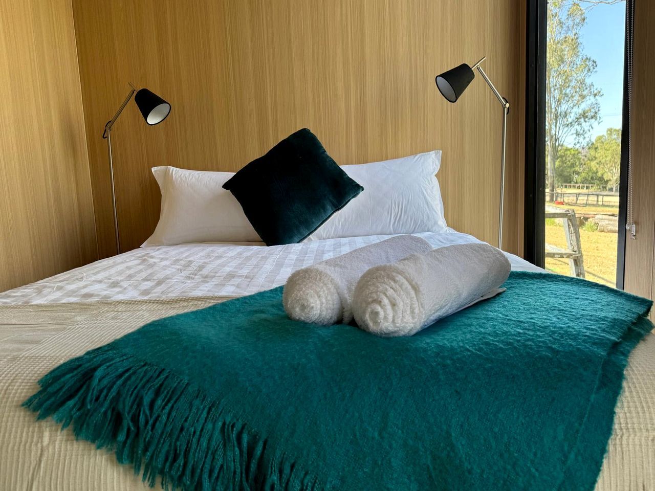 Een netjes opgemaakt bed met witte beddengoed, een turquoise plaid en opgerolde handdoeken.