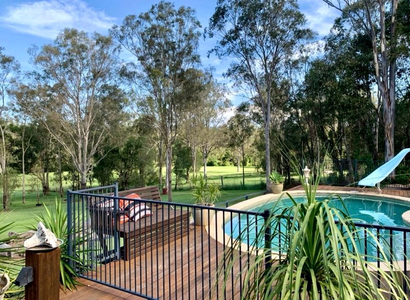 Uma área de piscina com deck de madeira, cercada por árvores e um gramado.