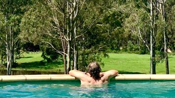 Pessoa relaxando em uma piscina com vista para árvores e um gramado.
