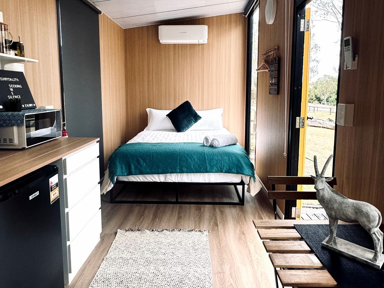 A compact bedroom with a bed, a small kitchenette, and a view of the outdoors.