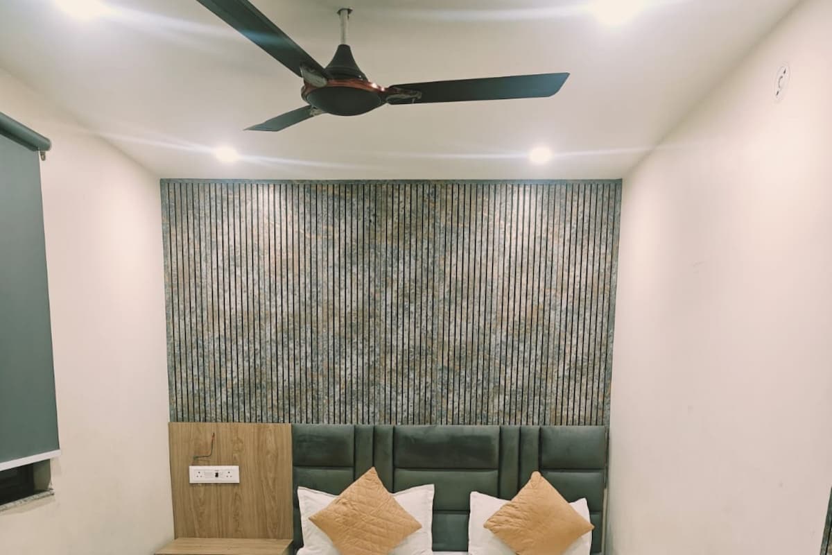 A hotel room with a bed, a bedside table, a chair, a ceiling fan, and a wall with vertical lines.