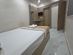 A hotel room with a bed, a wooden wardrobe, a television, and a bathroom door. - Shree Sai Lodge (Prayagraj)