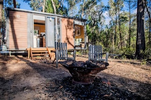 Uma cabana com porta aberta, um braseiro e um banco na parte externa.