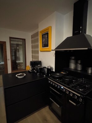 Eine Küche mit einem schwarzen Herd, einer Kaffeemaschine und einem Toaster. An der Wand hängt ein gerahmtes Bild.