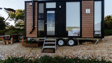 Uma casa móvel moderna com porta deslizante, um pequeno alpendre e entrada por um caminho de cascalho.