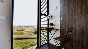 Una habitación con vista a un paisaje rural, una mesa de madera con un florero y una silla.