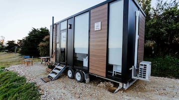 Une maison mobile moderne, dotée d’un toit plat, de grandes fenêtres et d’un petit espace extérieur aménagé pour s’asseoir.