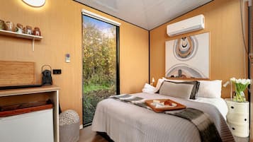 A modern bedroom with a bed, bedside table, and a view of greenery through a sliding door.