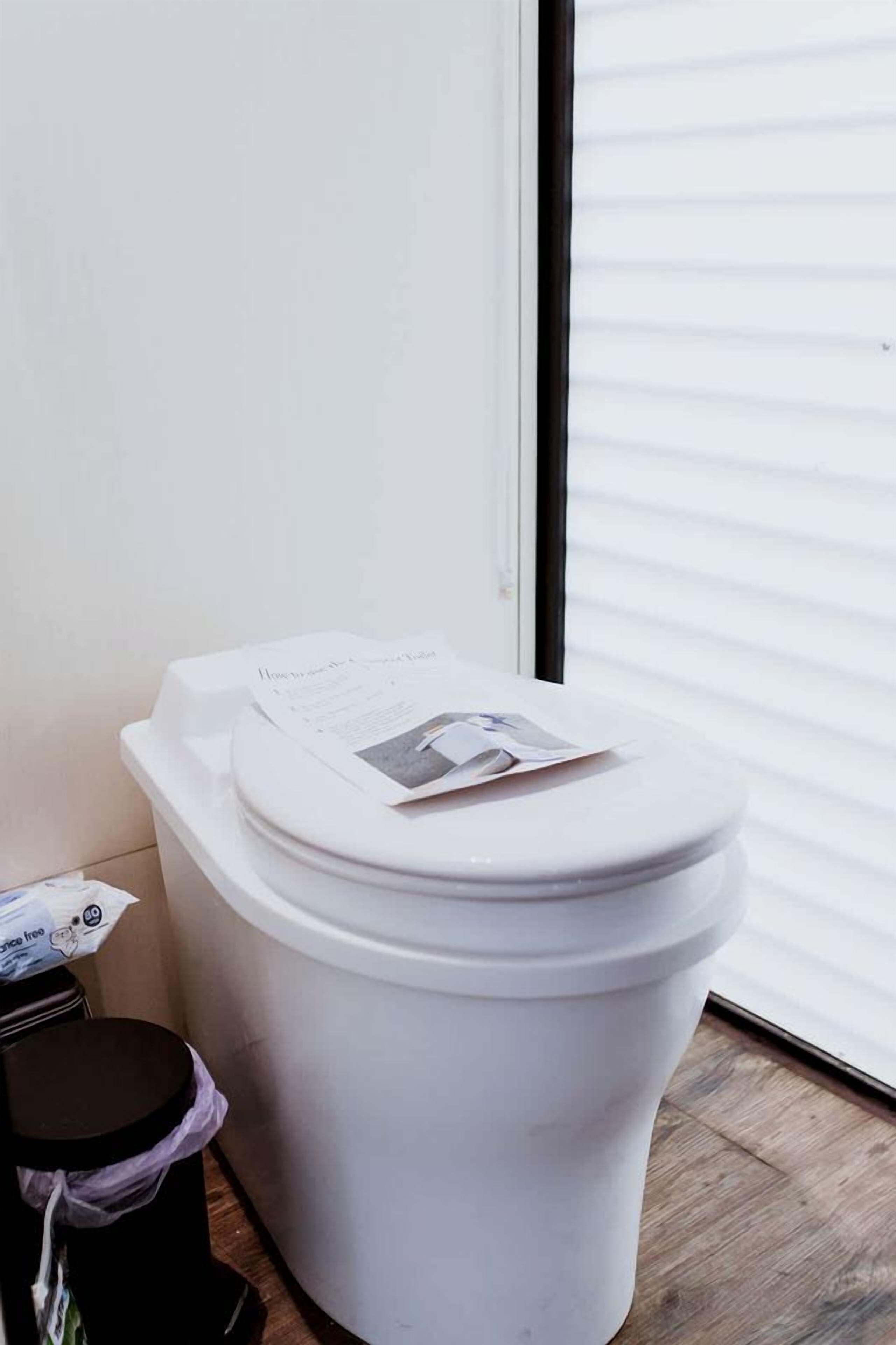 A white toilet with a lid, a black trash bin, and a small black stool.