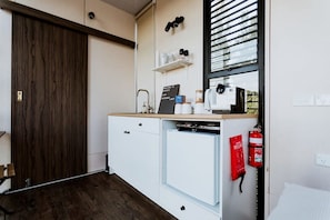 A compact kitchenette with a coffee machine, a small refrigerator, and a fire extinguisher.