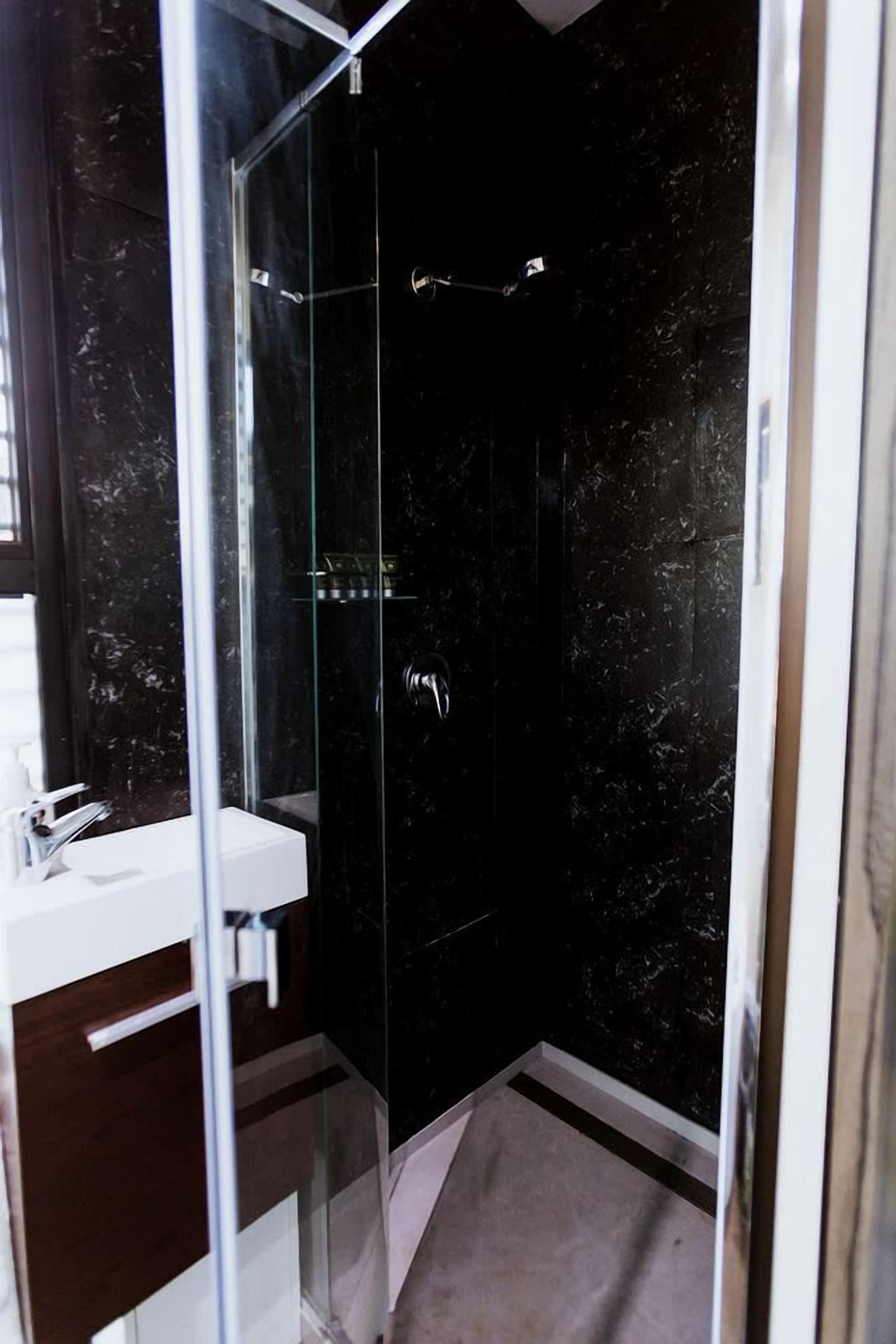 A modern bathroom with a glass-enclosed shower, a white sink, and dark marble walls.