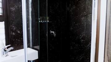A modern bathroom with a glass-enclosed shower, a white sink, and dark marble walls.