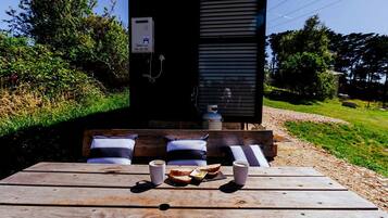 A wooden deck with a table set for two, a bench with pillows, and a gas cylinder.