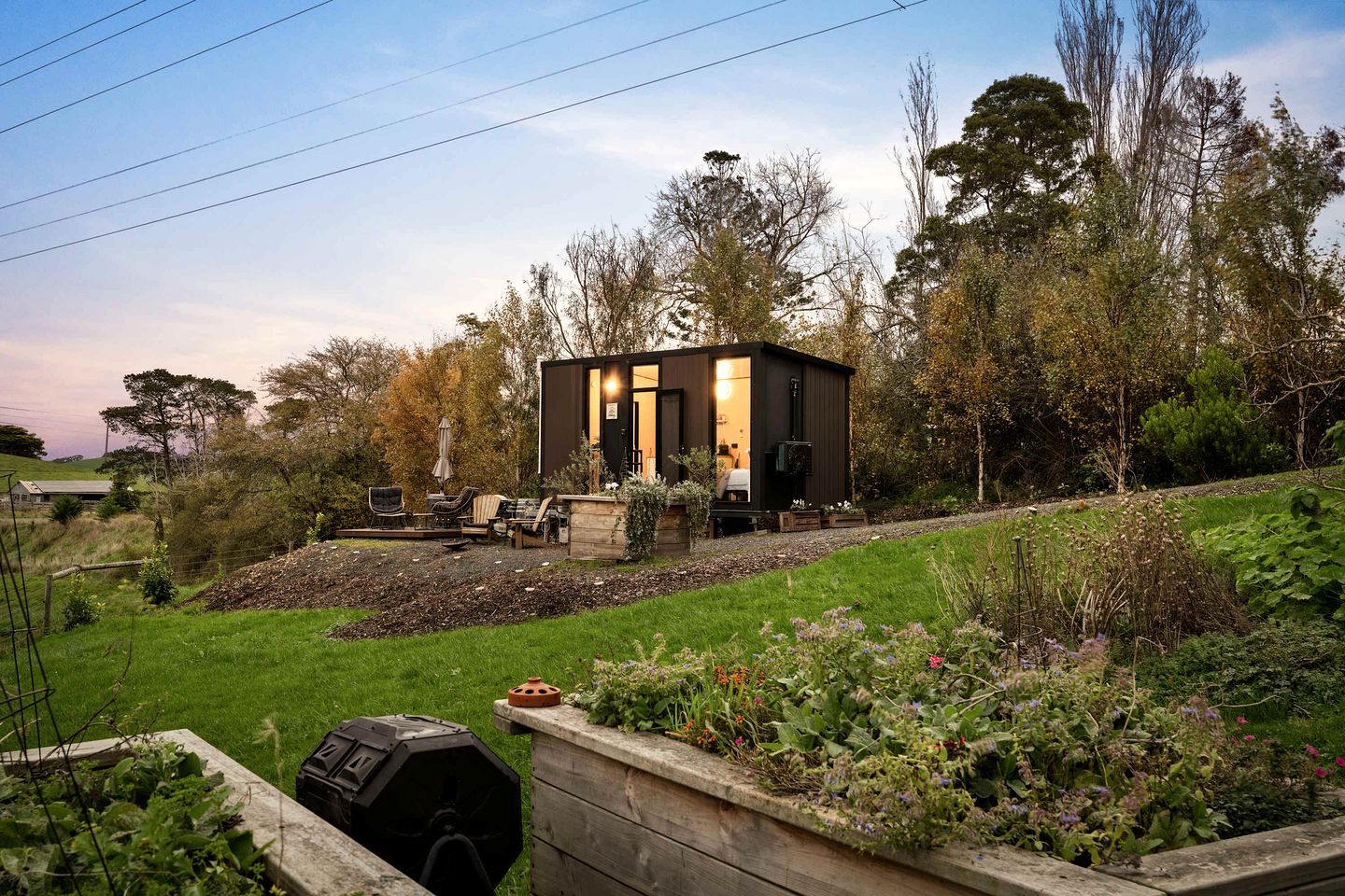 Une petite cabane de couleur sombre, dotée d’une entrée bien visible et d’un espace patio aménagé avec du mobilier d’extérieur.
