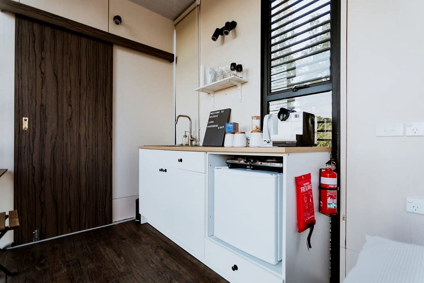 A compact kitchenette with a coffee machine, a small refrigerator, and a fire extinguisher.