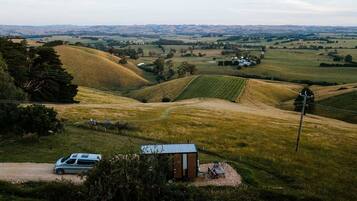 A rural landscape with rolling hills, a small cabin, and a parked vehicle.