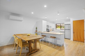 A modern kitchen with white cabinets, a wooden dining table, and bar stools. - Hat Huts 40 Hutcheson St Hat Head (Hat Head)