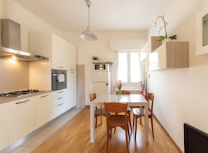 A modern kitchen with white cabinetry, a dining table with chairs, and a hanging pendant light. - HouSmart Risorgimento 9 (Riale)